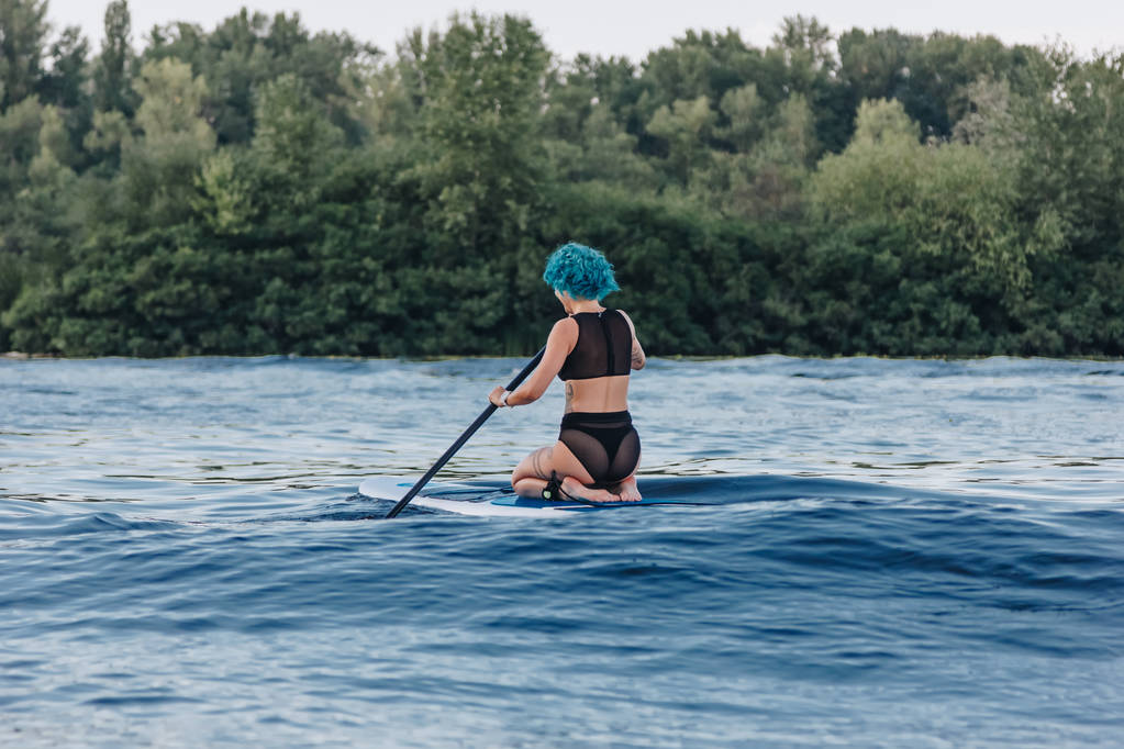 vista trasera de la chica con el pelo azul sentado en el tablero de paddle en el río
 - Foto, Imagen