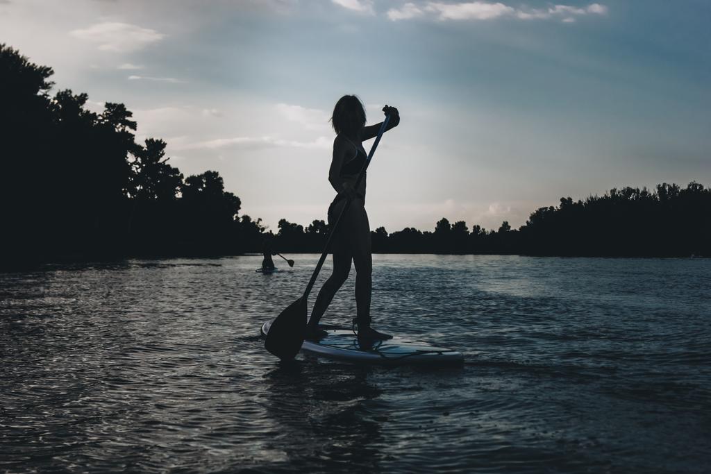 silhouette of athletic woman standup paddleboarding on river - Photo, Image