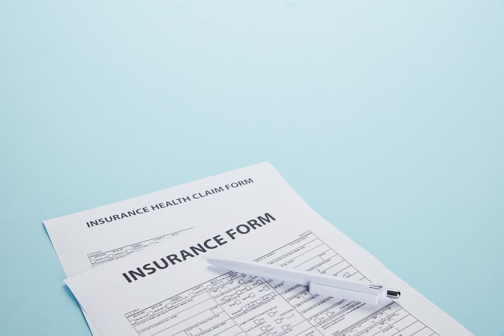 vista de cerca del formulario de seguro, del formulario de solicitud de seguro de enfermedad y de la pluma aislados en azul
 - Foto, imagen