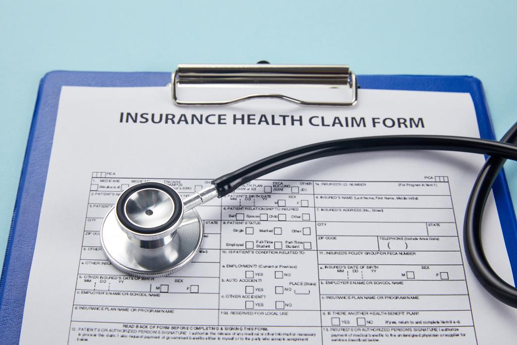 Nahaufnahme des Versicherungsantragsformulars auf Klemmbrett und Stethoskop auf blau   - Foto, Bild