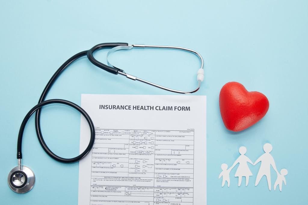 pohled shora na formulář žádosti o pojištění zdravotní, papír řez rodinu, symbol červené srdce a stetoskop na modré  - Fotografie, Obrázek