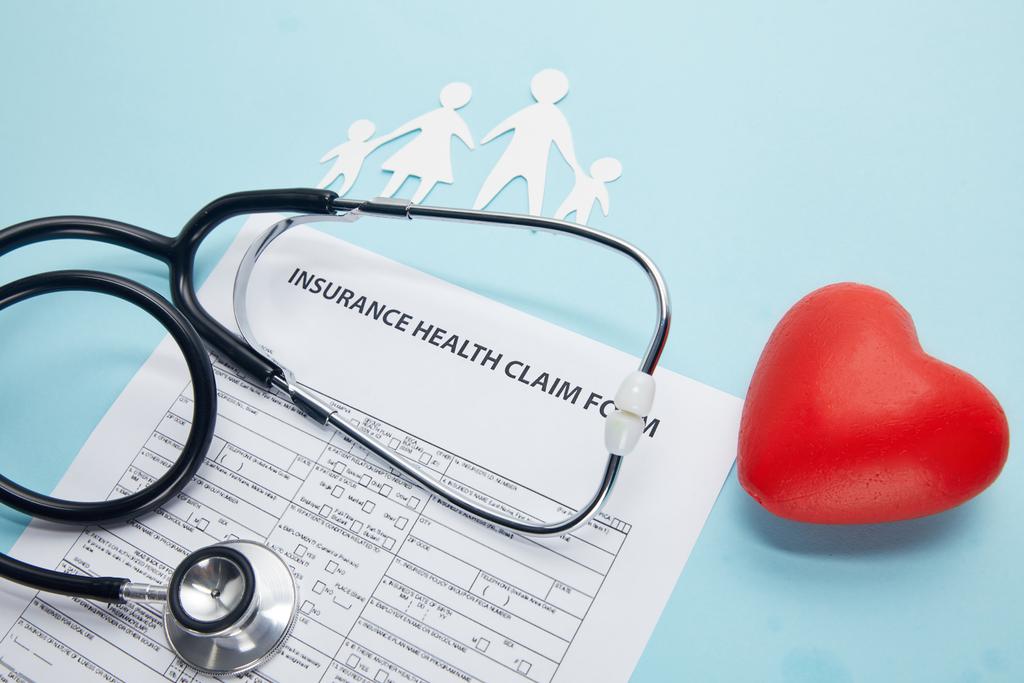 Detailní pohled formulář žádosti o pojištění zdravotní, papír řez rodinu, symbol červené srdce a stetoskop na modré - Fotografie, Obrázek