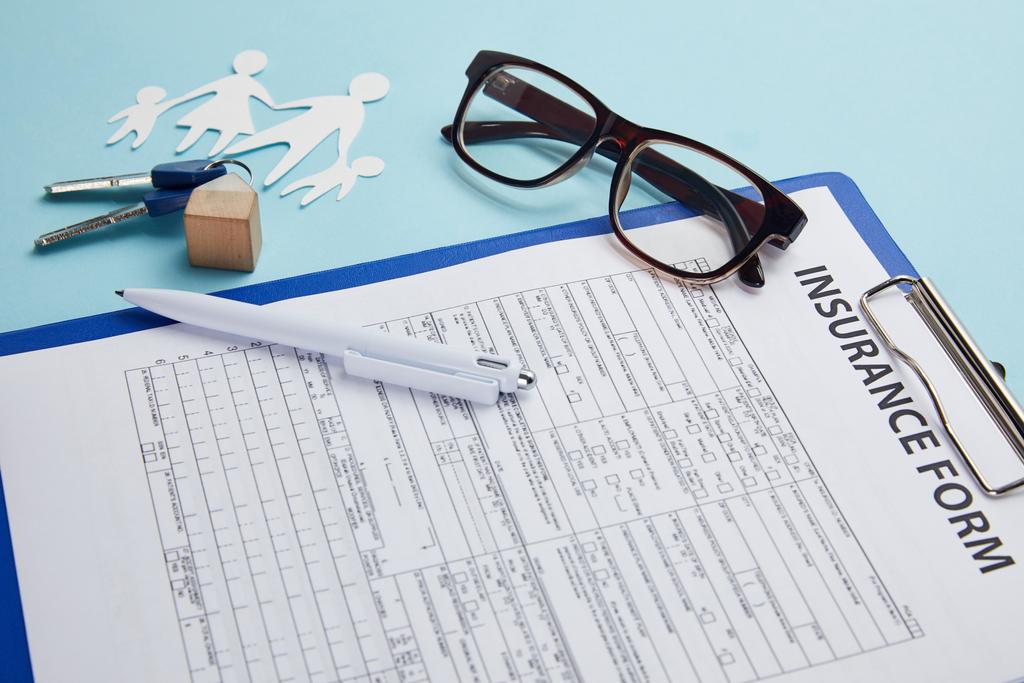verzekeringsformulier, brillen, pen, papier knippen van familie en sleutels geïsoleerd op blauw     - Foto, afbeelding