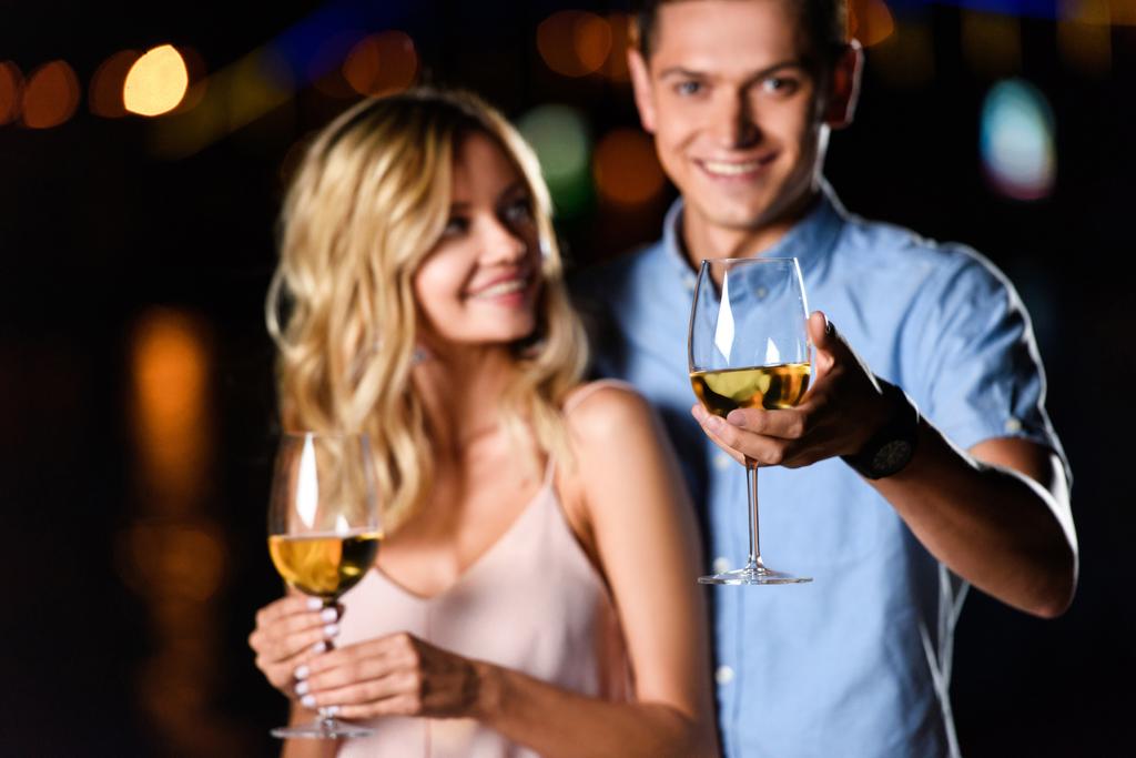selective focus of young couple holding glasses of wine on river beach in evening - Photo, Image