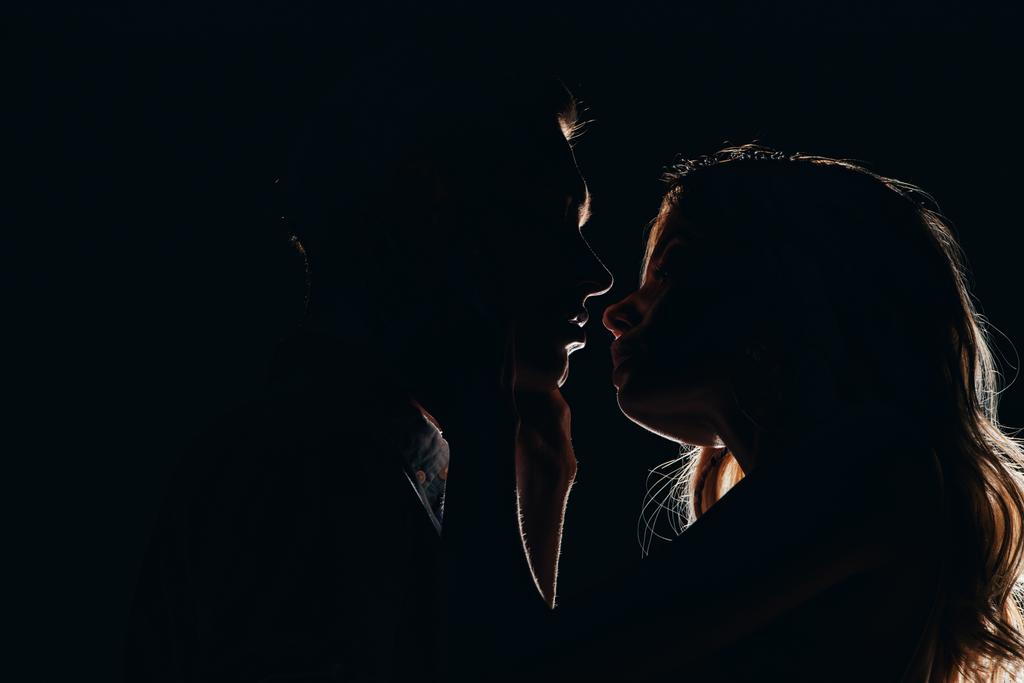 silhouettes of boyfriend and girlfriend going to kiss in dark - Photo, Image