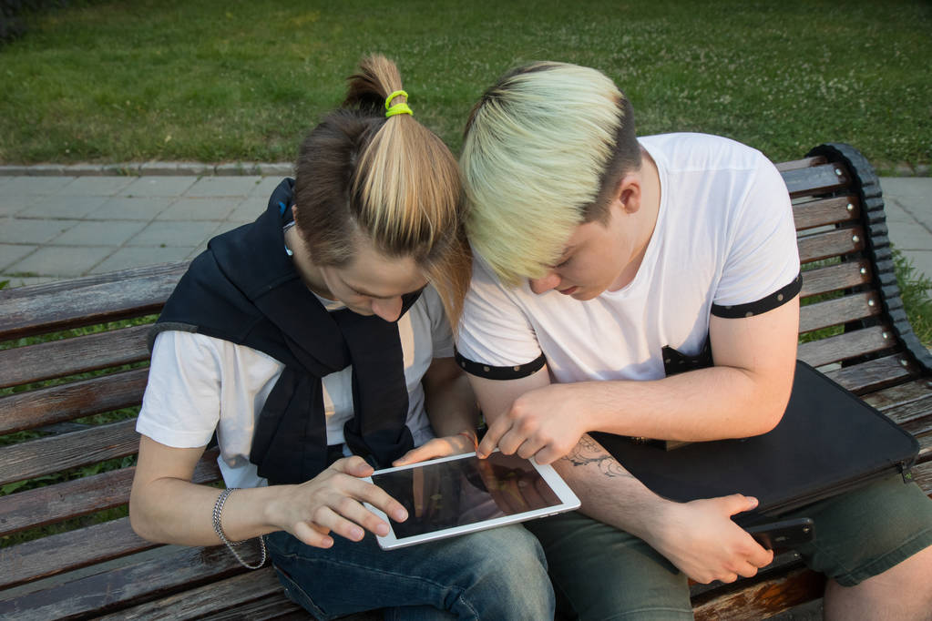 Dos amigos sentados en el banco en el parque y viendo la tableta. Diviértete en línea
.  - Foto, imagen