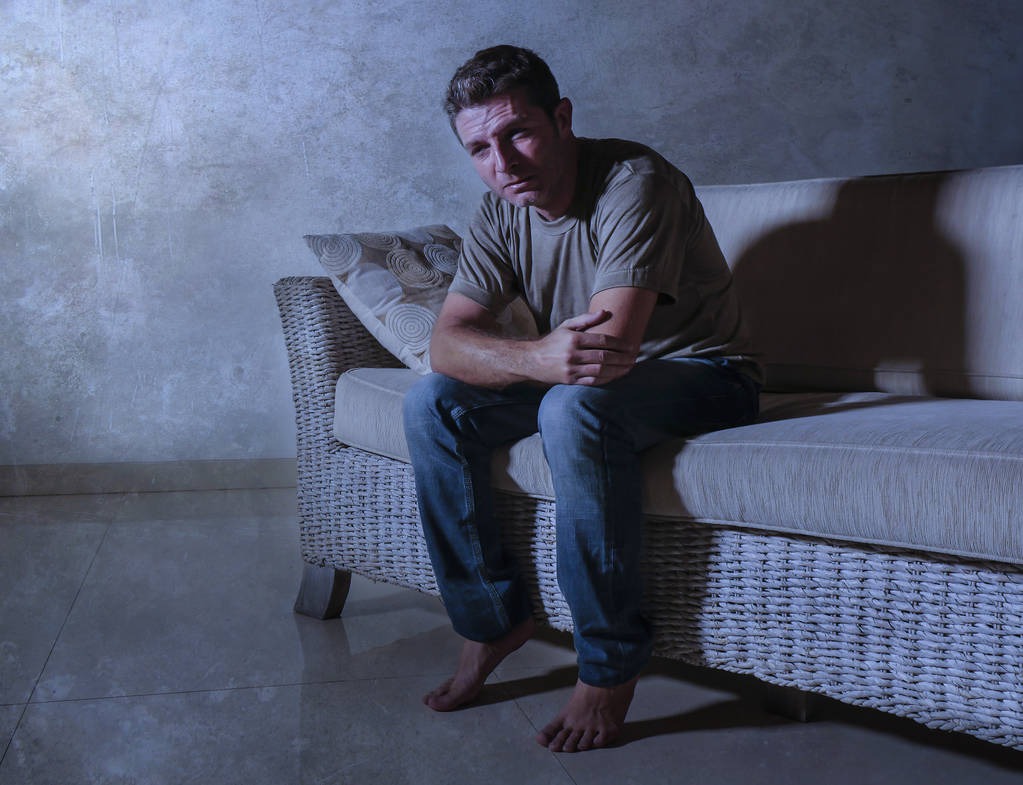 dramatyczne światła portret styl życia, młody człowiek smutny i przygnębiony siedzący w zacienionym domowej kanapie w bólu i depresji uczucie podkreślił i rozpaczliwy płacz sam cierpienia kryzys lęk - Zdjęcie, obraz