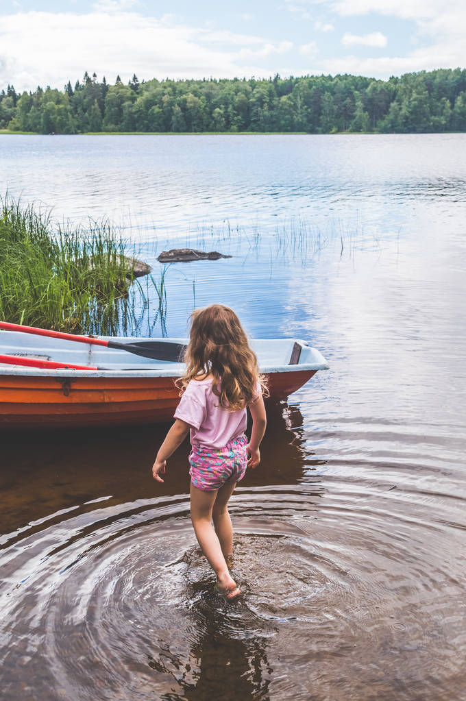 Tyttö, lapsi kävelee veden, järven, joen, lähellä veneen metsässä
 - Valokuva, kuva