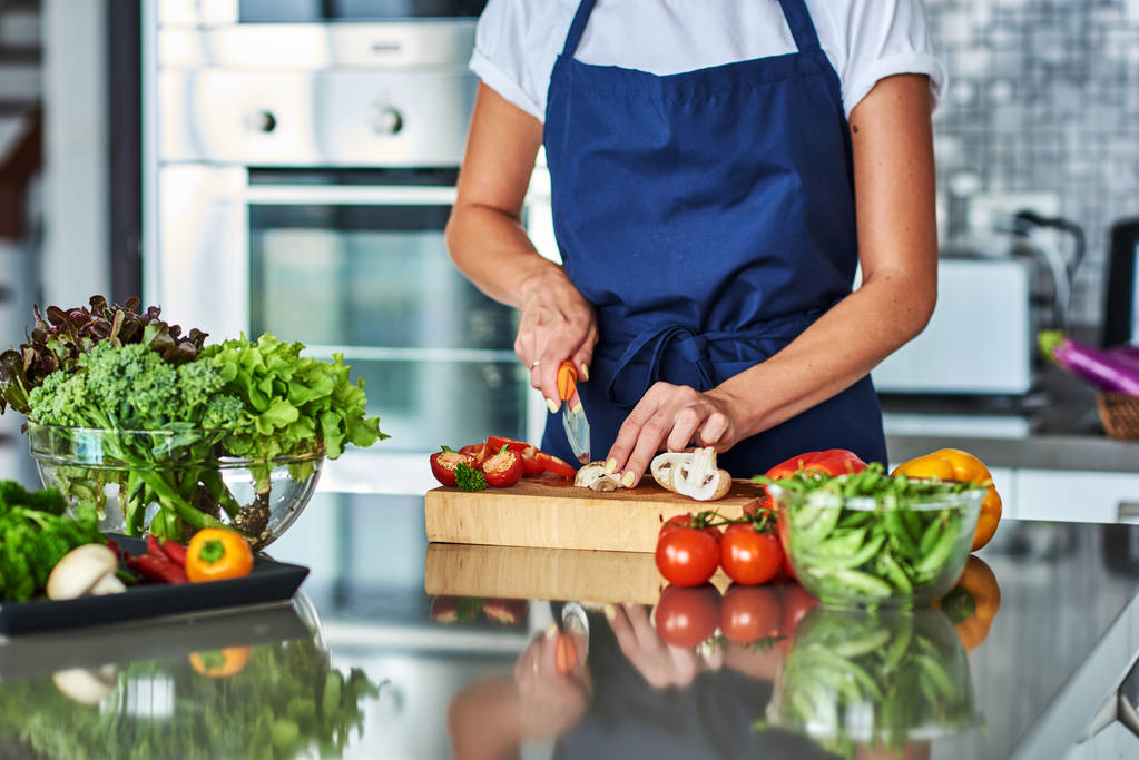 Mano de una mujer ama de casa preparando la cena, verduras: tomates, pimientos, lechuga en una tabla de cortar en la cocina
. - Foto, imagen