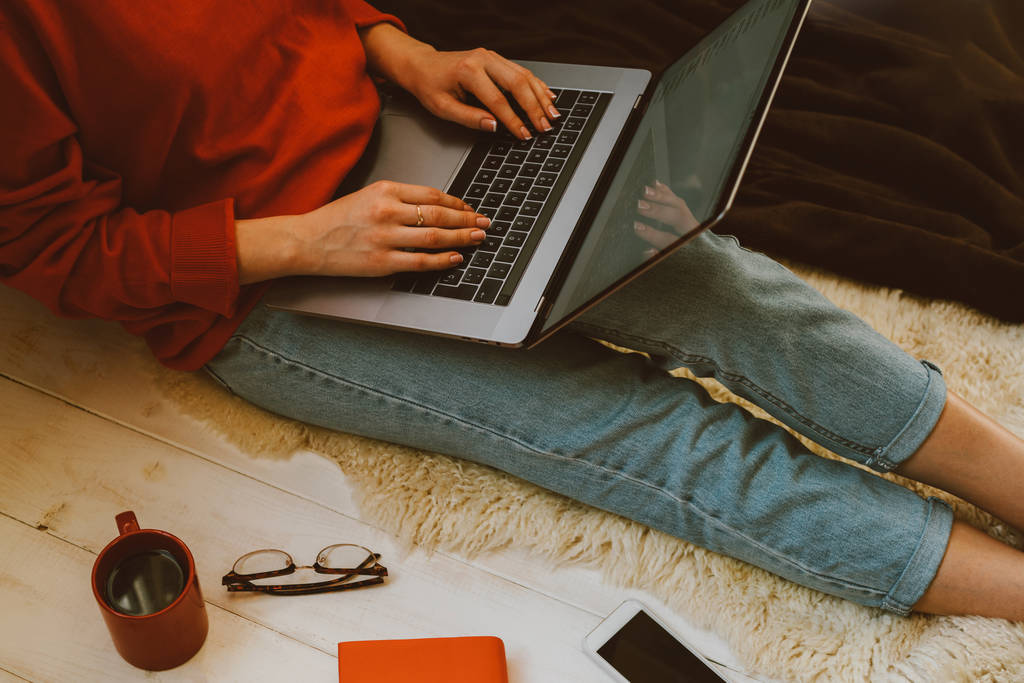 Widok z góry z młodą kobietę trzyma laptopa na kolanach, siedząc w domu. Kobieta korzysta z laptopa do przeglądania sklepu internetowego. Zakupy online koncepcja. Młoda kobieta siedzi na dywanie w domu - Zdjęcie, obraz