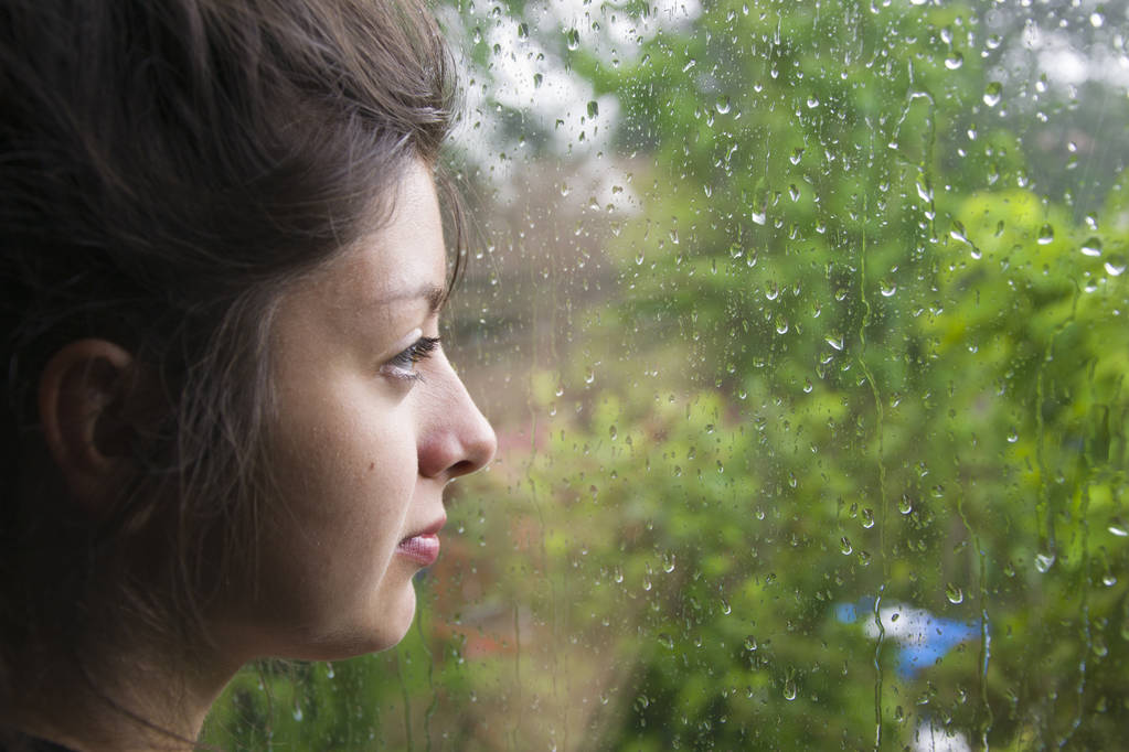 Sad κορίτσι μοιάζει έξω από το παράθυρο και βρέχει. Γυναίκα με ωραίο αναζητούν ακούω - Φωτογραφία, εικόνα