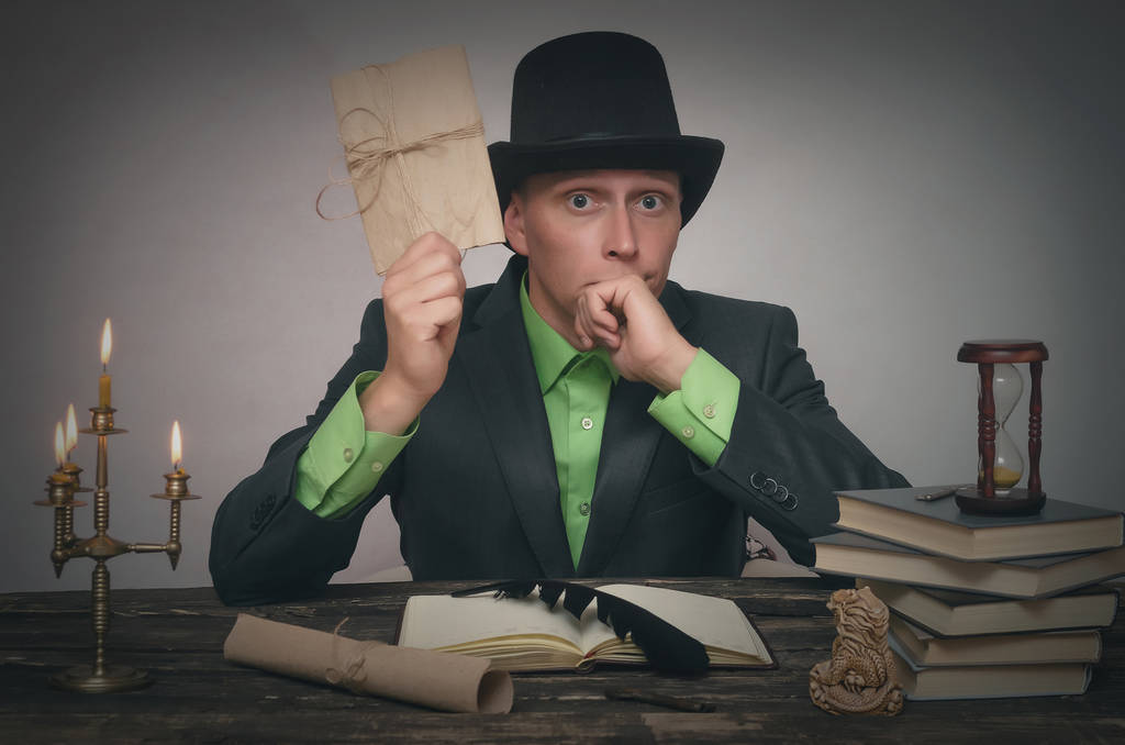 Mann mit Melone und Anzug sitzt am Tisch und hält eine Urkunde in der Hand. Schriftsteller, Autor, Detektiv oder Agentenkonzept. - Foto, Bild