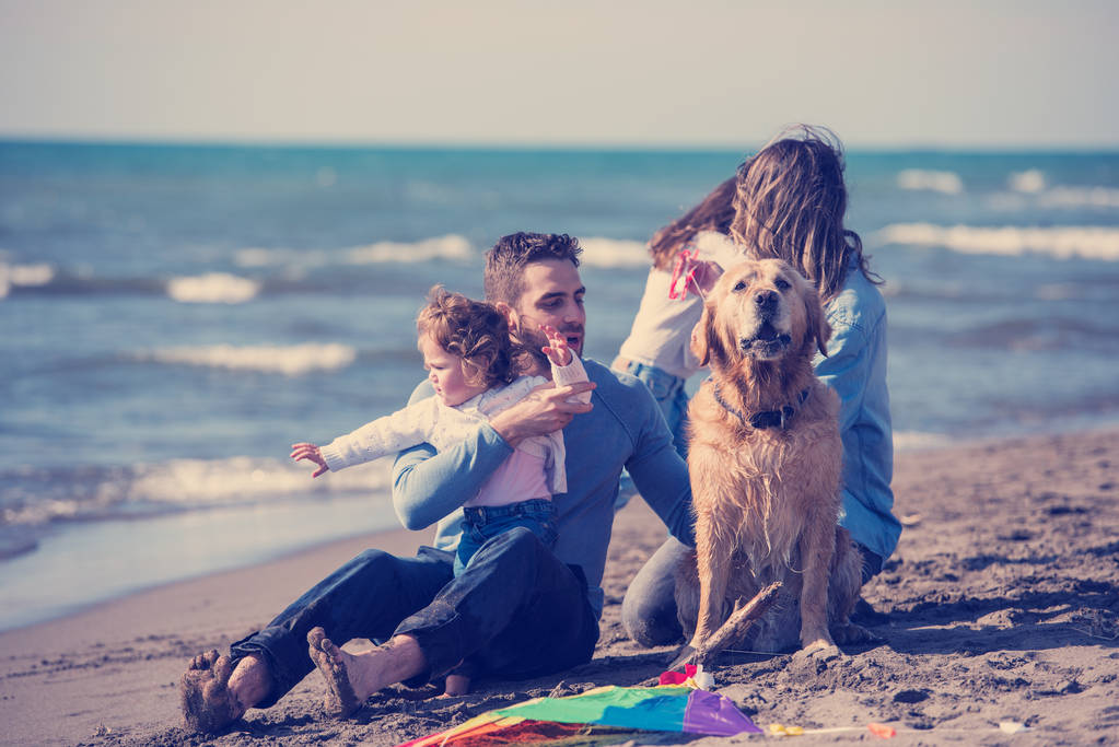 秋の日のフィルターの間にビーチで犬と凧で楽しんでいる子供たちと幸せな若い家族 - 写真・画像