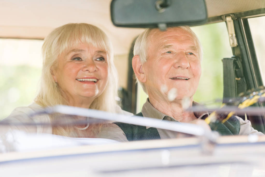 Frontansicht eines glücklichen Senioren-Paares am Steuer eines beigefarbenen Autos - Foto, Bild