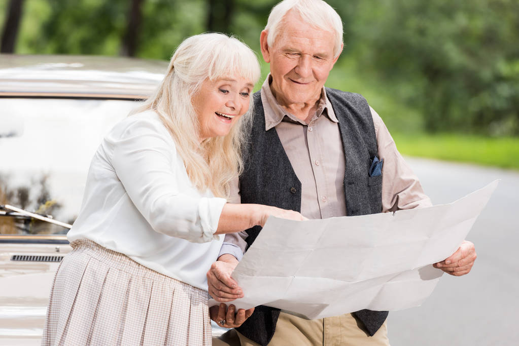 feliz pareja de ancianos sosteniendo mapa y apoyándose en el coche retro
 - Foto, imagen