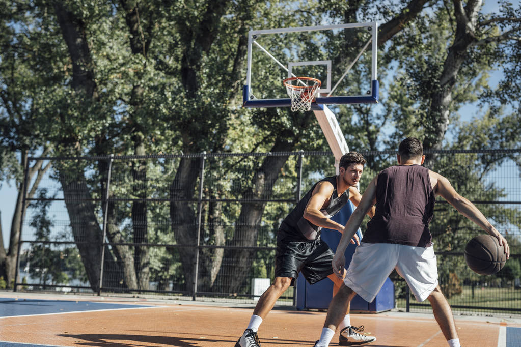 Δύο νεαροί άνδρες που παίζει μπάσκετ στο υπαίθριο γήπεδο. - Φωτογραφία, εικόνα