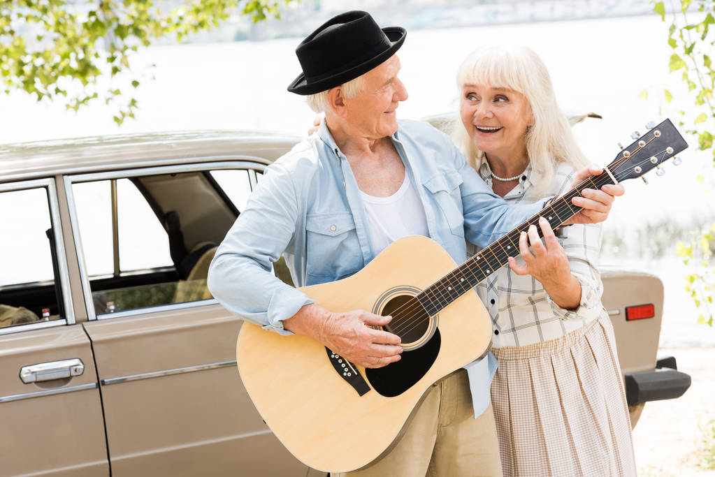 mari aîné et femme regardant l'autre et jouant de la guitare contre la voiture beige
 - Photo, image