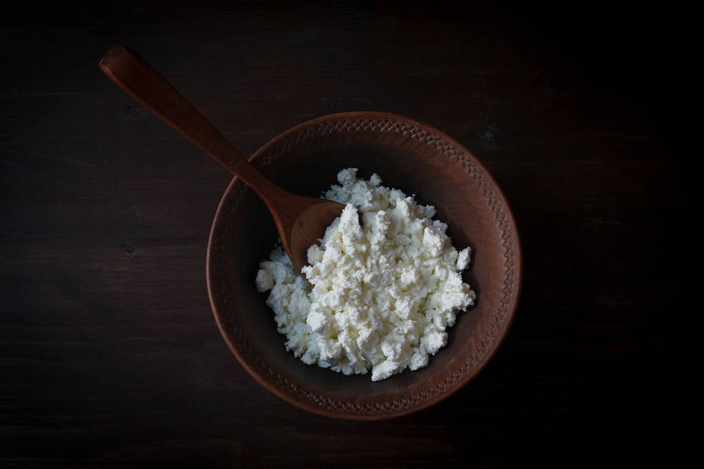Cup of cottage cheese, wooden spoon on dark wooden background. The view from the top. - Photo, Image