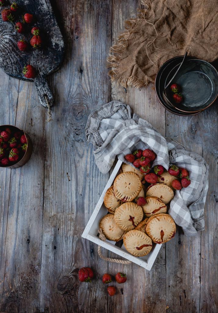 elevated view of tasty cookies with strawberries in tray on wooden table - Photo, Image
