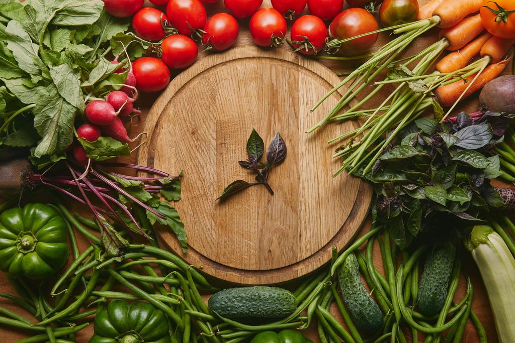 Vielfalt an frischem Gemüse und Kräutern durch Schneidebrett auf Holztisch - Foto, Bild