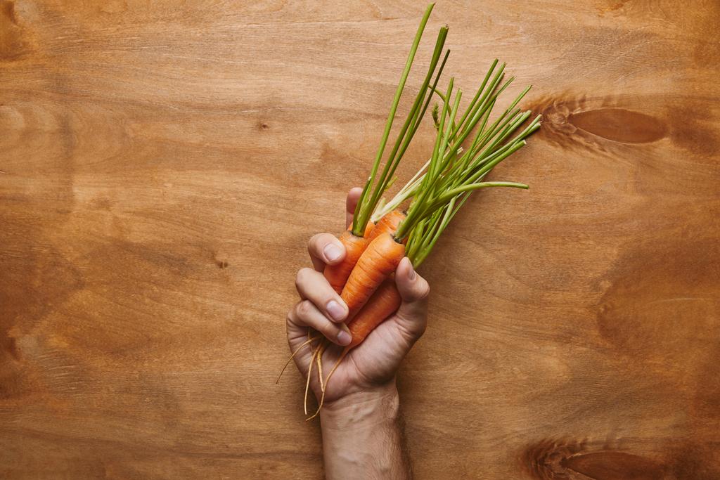 Мужская рука с органической морковью на деревянном столе
 - Фото, изображение