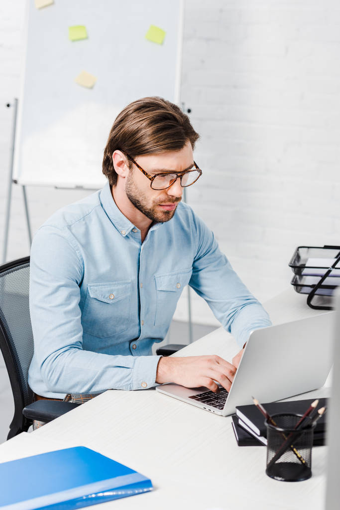 концентрований молодий бізнесмен, який працює з ноутбуком в сучасному офісі
 - Фото, зображення