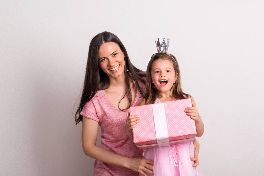 Una niña pequeña con diadema de corona y su madre sosteniendo un regalo en un estudio
. - Foto, Imagen