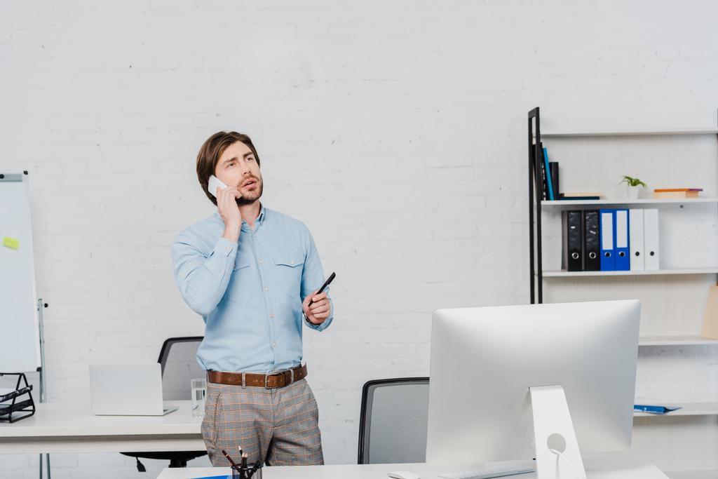 jeune homme d'affaires émotionnel levant les yeux tout en parlant par téléphone au bureau moderne
 - Photo, image