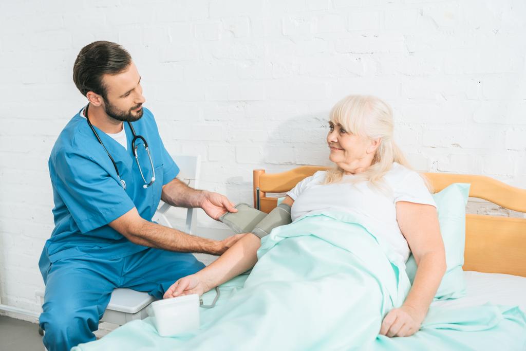 joven trabajadora social midiendo la presión arterial a una mujer mayor acostada en la cama
 - Foto, Imagen