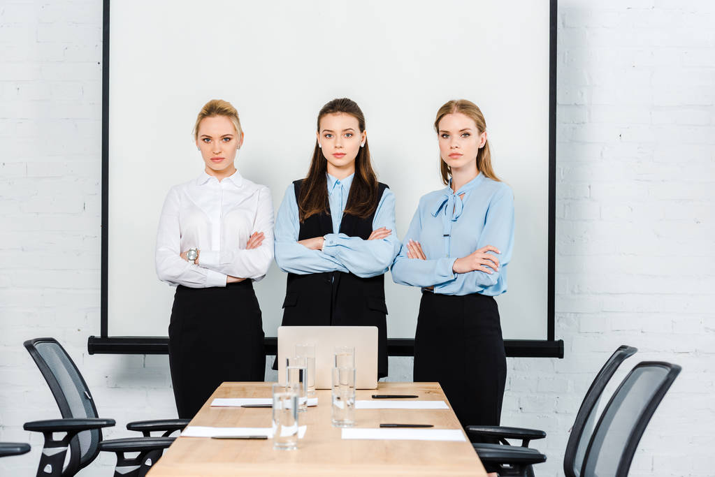 attractive young businesswomen with crossed arms looking at camera at conference hall - Photo, Image
