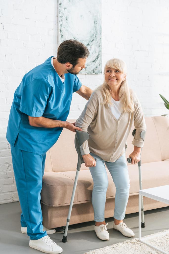 infermiera di sesso maschile che sostiene sorridente donna anziana con stampelle
 - Foto, immagini