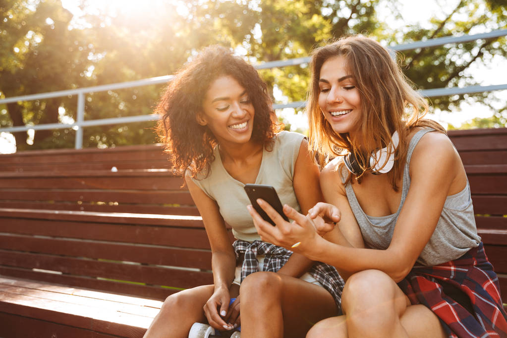 Deux jeunes filles excitées s'amusent ensemble tout en utilisant un téléphone portable au parc
 - Photo, image