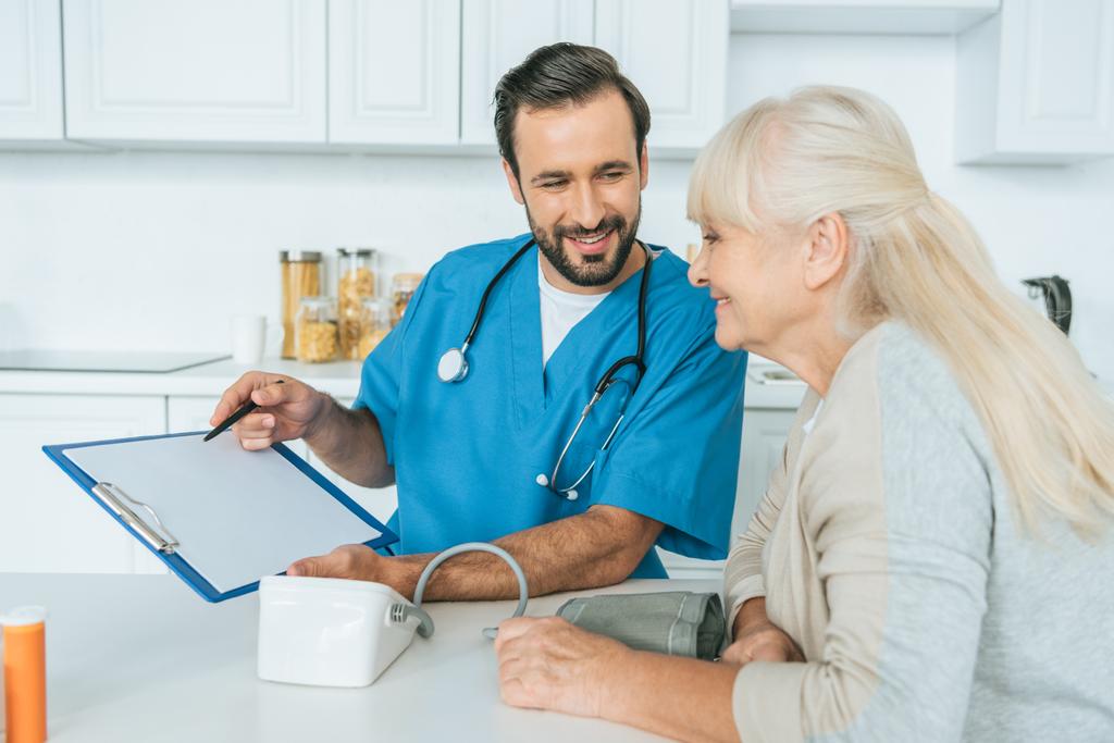 enfermeiro sorridente mostrando prancheta para a mulher idosa feliz depois de medir a pressão arterial
 - Foto, Imagem