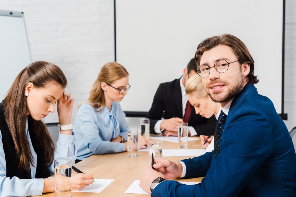 усміхнений молодий бізнесмен сидить у конференц-залі з колегами під час розмови
 - Фото, зображення