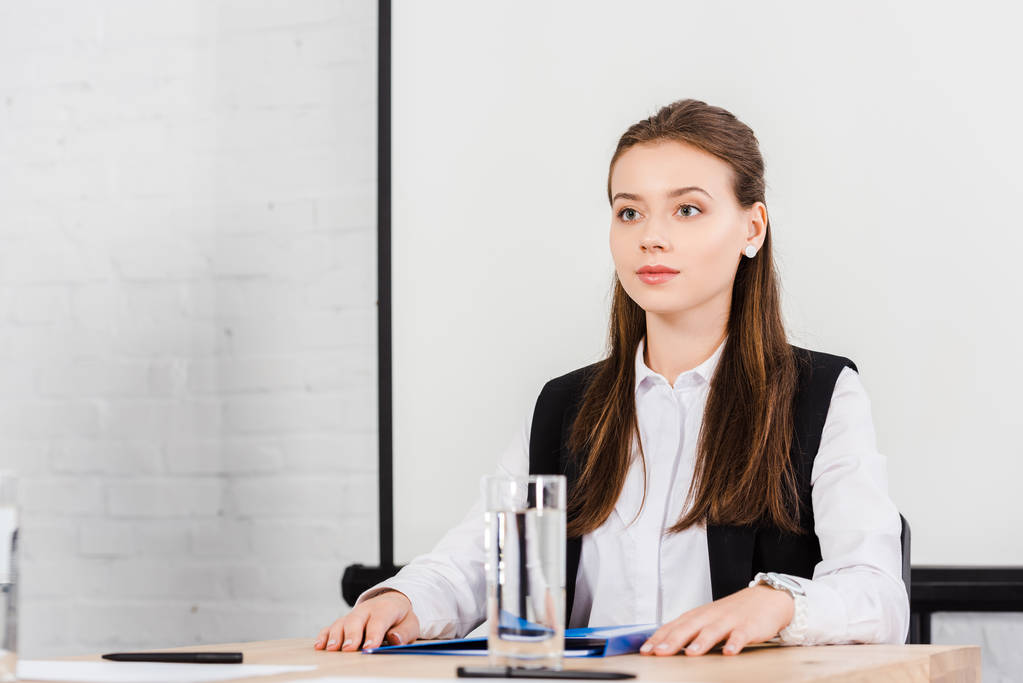 beautiful young businesswoman sitting at table in conference hall at modern office and looking away - Photo, Image