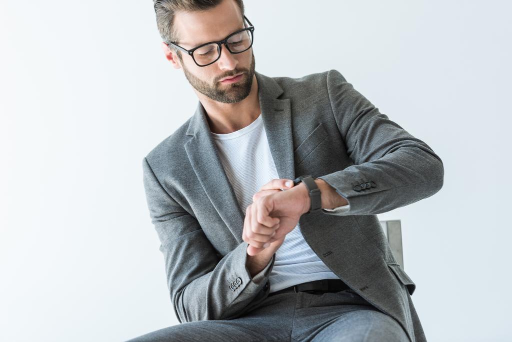 guapo barbudo hombre de negocios en traje gris mirando reloj, aislado en blanco
 - Foto, Imagen