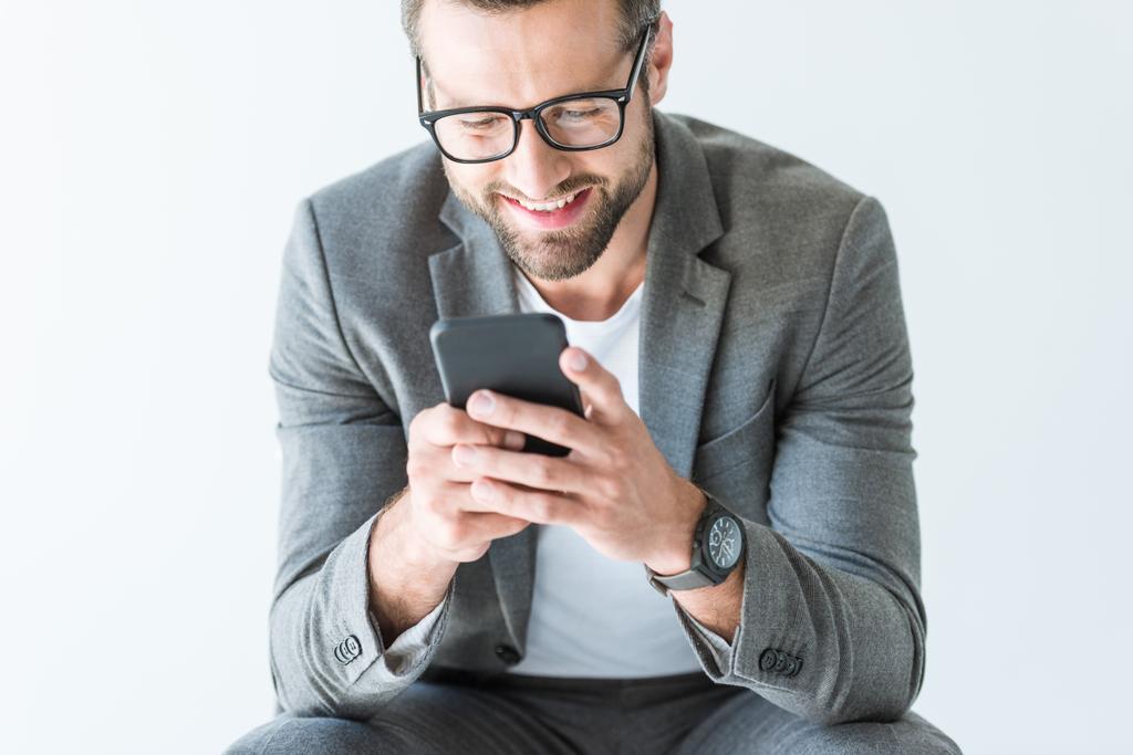 gri elbiseli smartphone, üzerinde beyaz izole kullanarak gülümseyen yakışıklı - Fotoğraf, Görsel