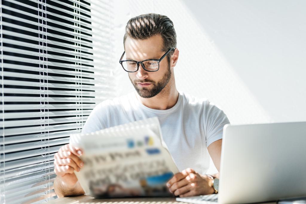 brunetta uomo leggendo giornale sul posto di lavoro con computer portatile
 - Foto, immagini