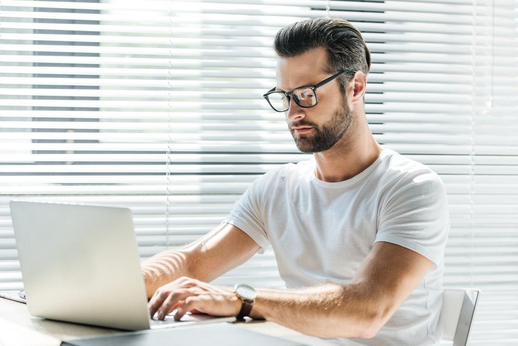 homme concentré dans les lunettes en utilisant un ordinateur portable sur le lieu de travail
 - Photo, image