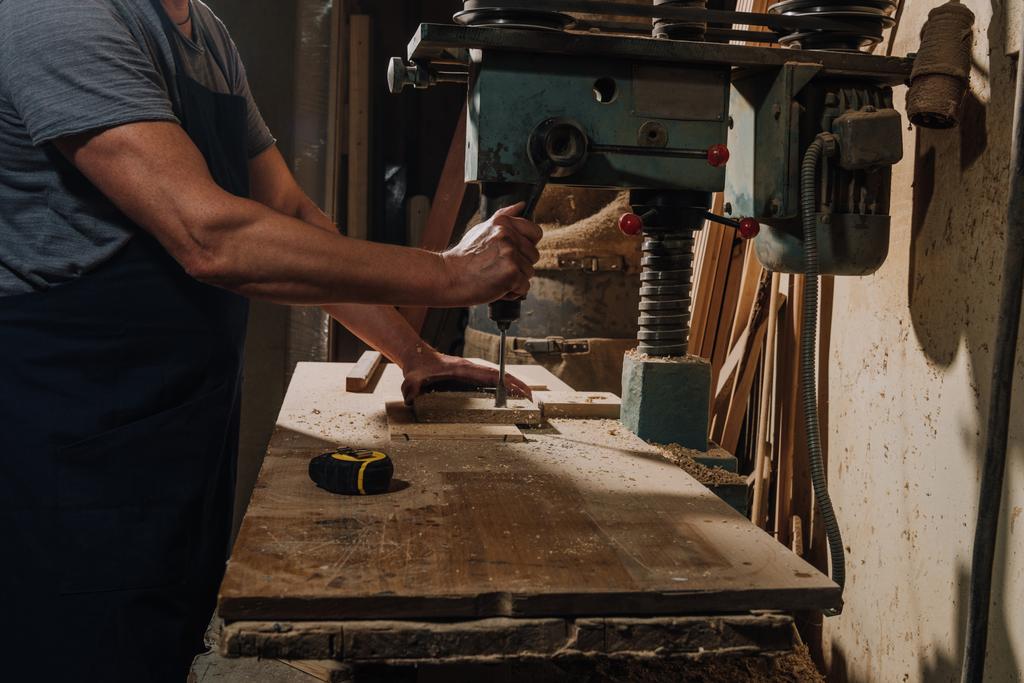 partial view of woodworker using electric drill on wood at workshop - Photo, Image