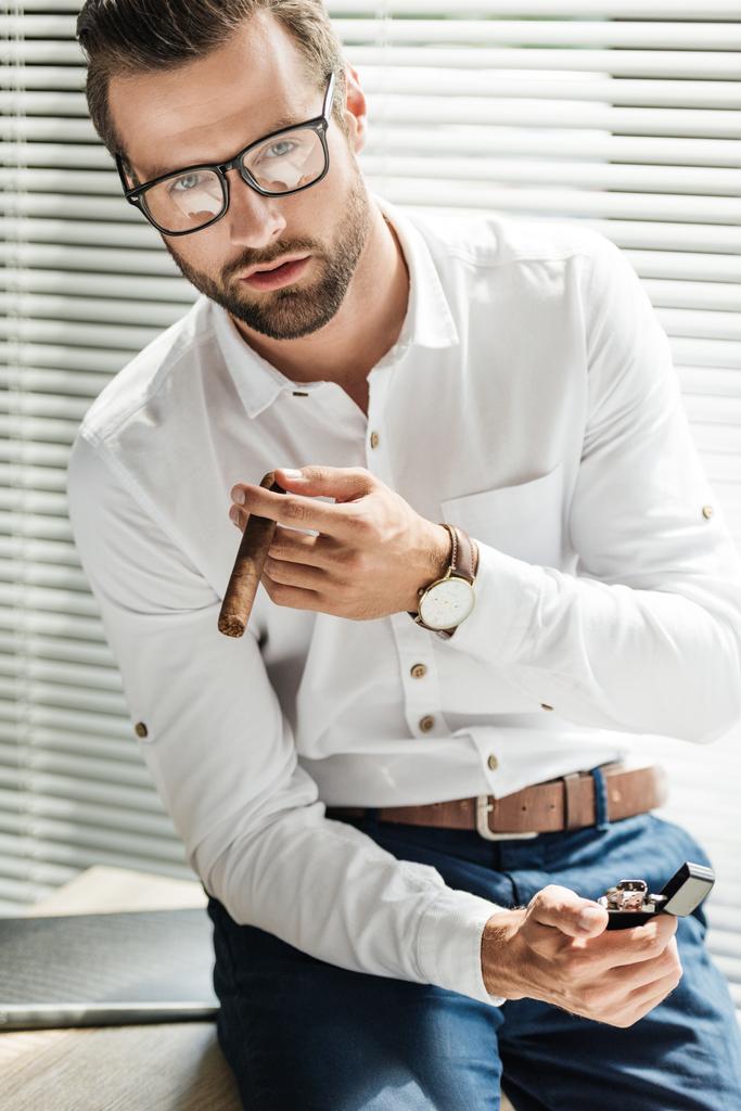 όμορφος γενειοφόρος επιχειρηματία σε γυαλιά με αναπτήρα το κάπνισμα πούρων - Φωτογραφία, εικόνα