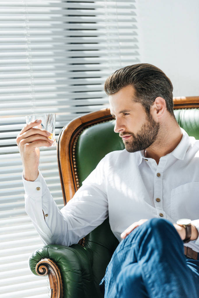uomo alla moda guardando vetro di whisky e seduto in poltrona
 - Foto, immagini