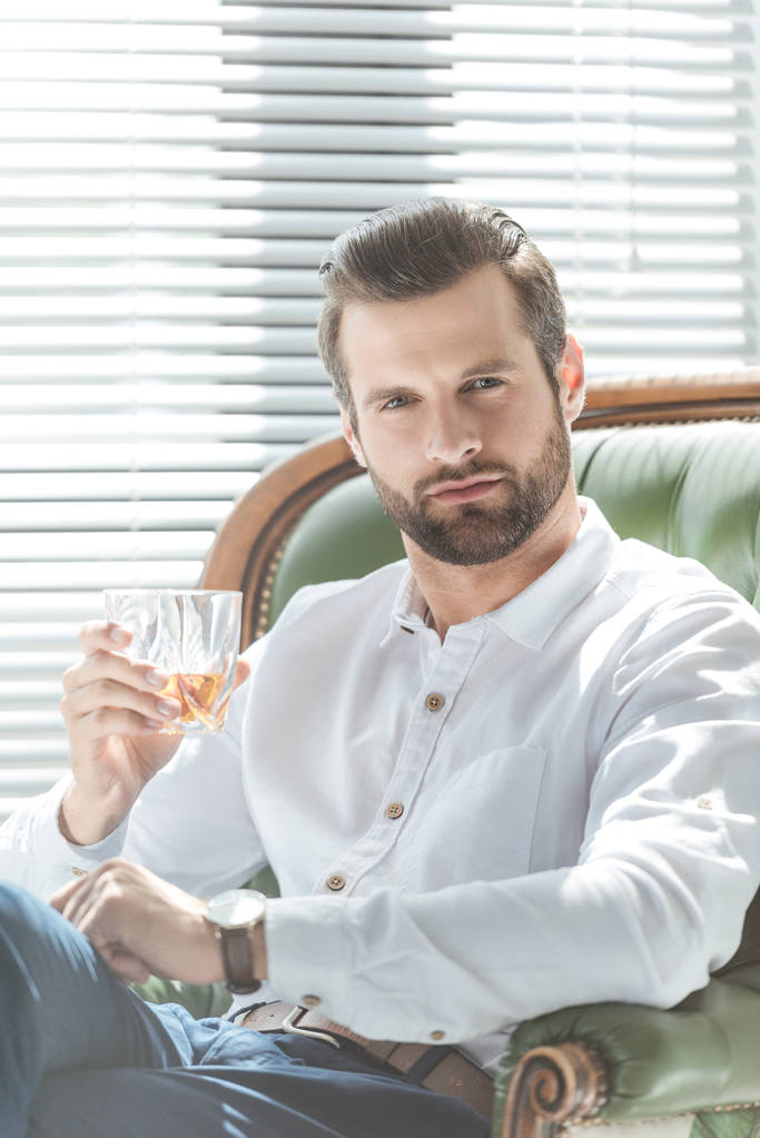 selbstbewusster, stilvoller Mann mit einem Glas Whiskey im Sessel - Foto, Bild
