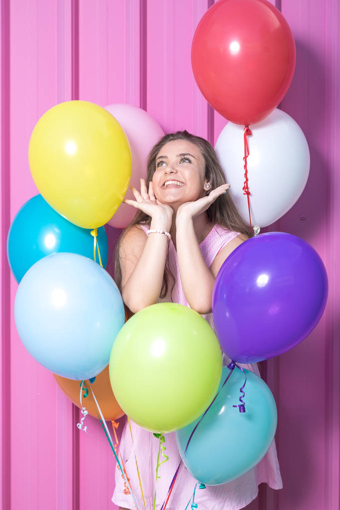 Mooie jonge vrouw met kleurrijke ballonnen op pastel roze achtergrond. - Foto, afbeelding