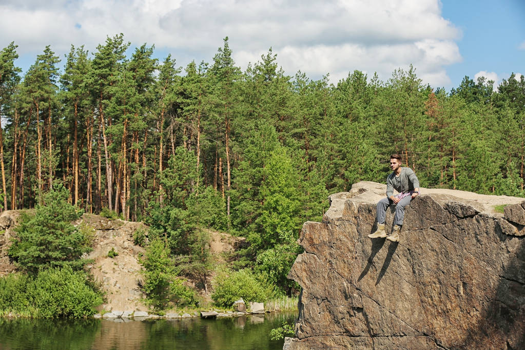 Nuori mies kalliolla lähellä järveä ja metsää. Leirintäaika
 - Valokuva, kuva