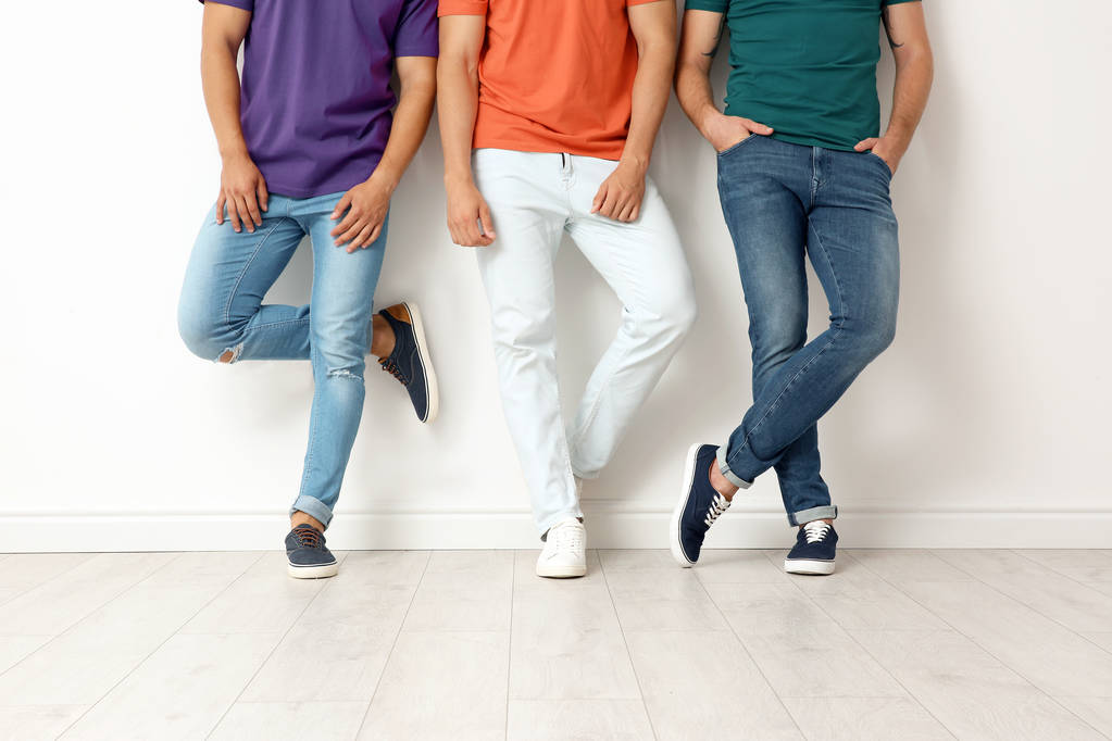 Groep van jonge mannen in jeans en kleurrijke t-shirts in de buurt van lichte muur - Foto, afbeelding