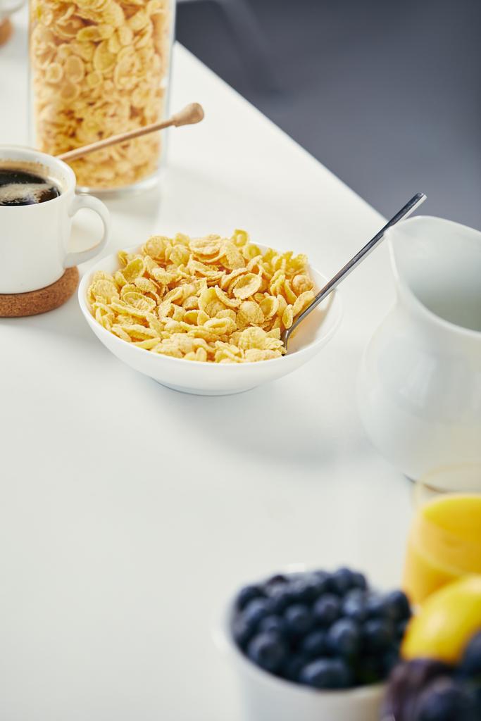 κλείνω πάνω θέα του μπολ νιφάδες καλαμποκιού και φλιτζάνι καφέ για πρωινό σε λευκή επιφάνεια - Φωτογραφία, εικόνα