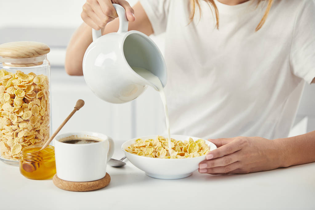 visão parcial da mulher derramando leite em tigela com flocos de milho durante o café da manhã em casa
 - Foto, Imagem