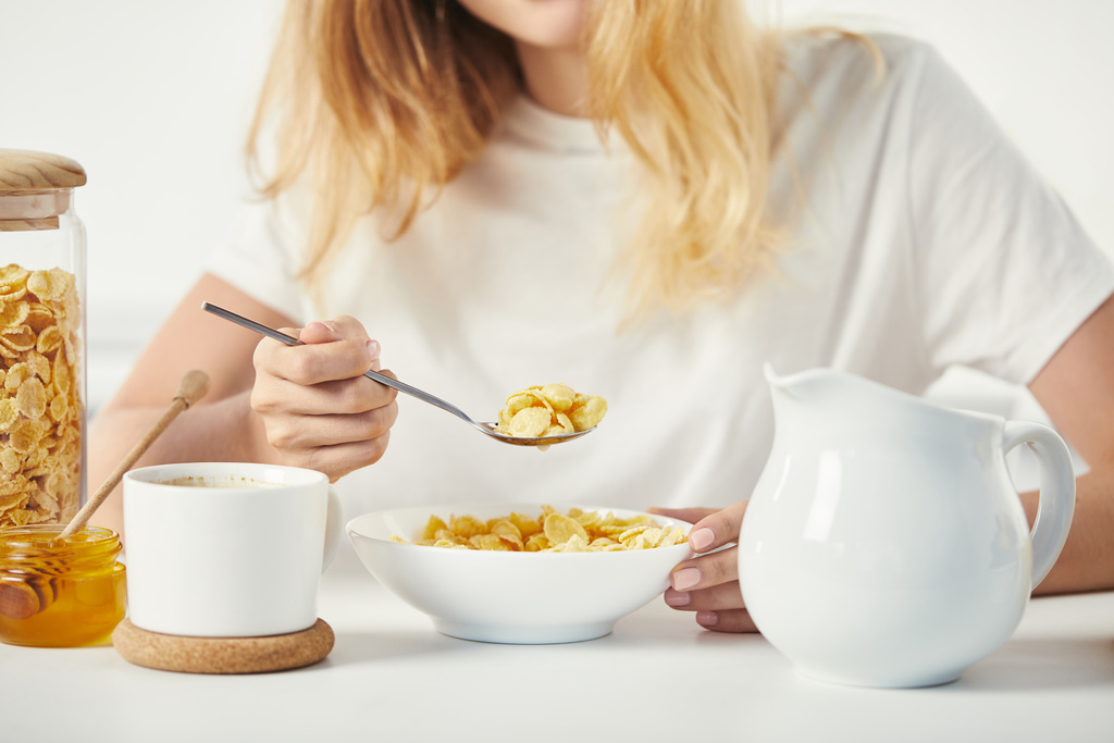 частичный вид женщины за столом с кукурузными хлопьями, медом и чашкой кофе на завтрак
 - Фото, изображение