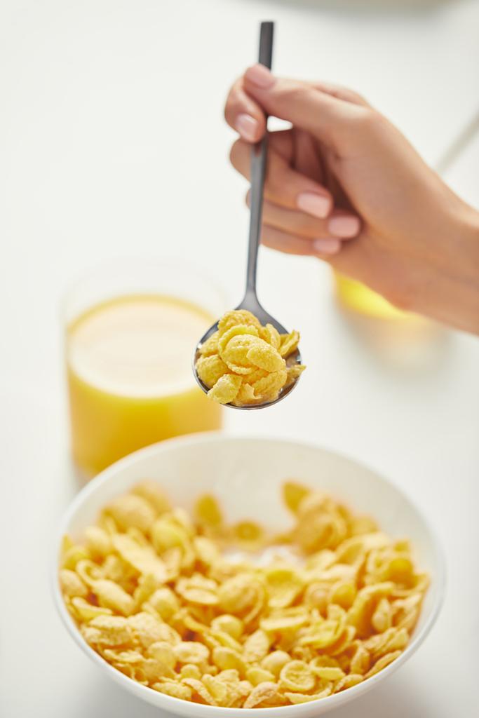 gedeeltelijke weergave van vrouw aan tafel met cornflakes en glas sap voor het ontbijt - Foto, afbeelding